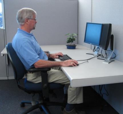Photo showing a person sitting at a desk, working on on a computer, from the side