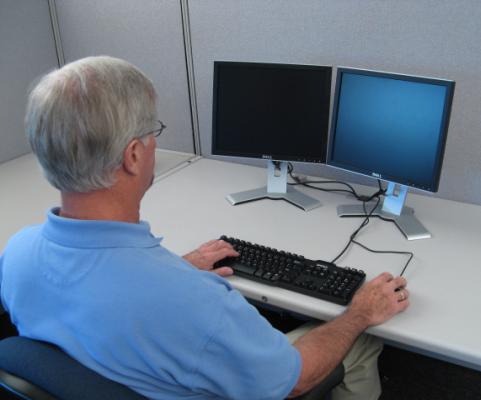 Photo showing a person sitting at a desk, working on on a computer, looking over the person's shoulder