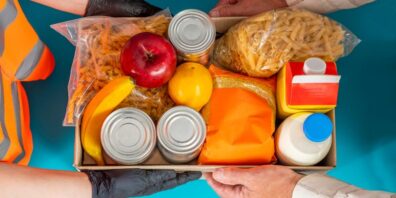 Foodbanks A box of food as seen from overhead, being passed from one pair of hands to another